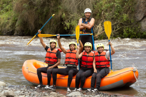 A team of paddlers sit atop a river raft with their trusty guide behind them.